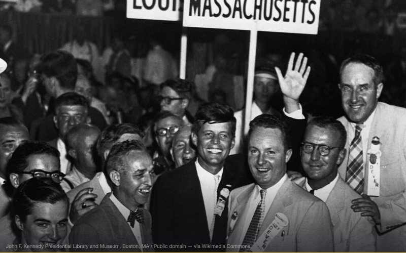 Congressman John F. Kennedy, with Massachusetts Delegates, standing in the middle of a crowd at the 1952 Democratic National Convention waving. — related to CIA Plot to Kill JFK