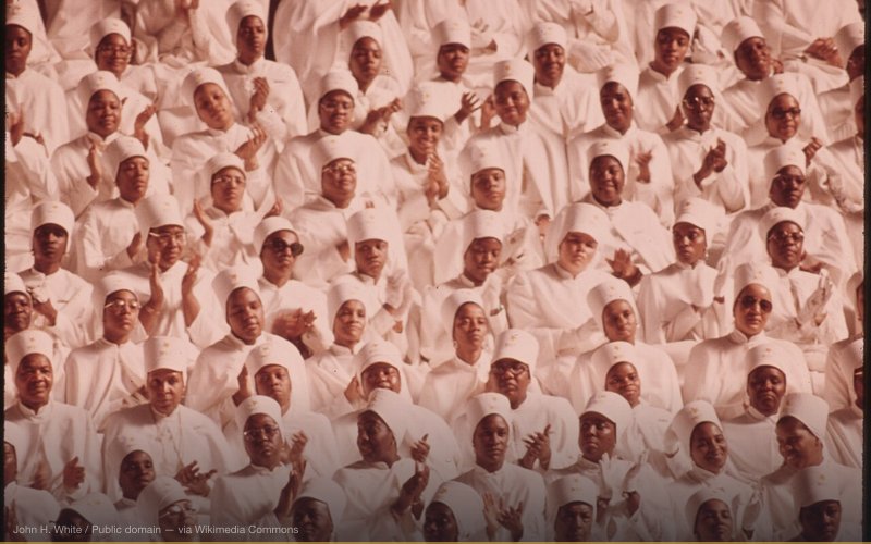 BLACK MUSLIM WOMEN DRESSED IN WHITE APPLAUD ELIJAH MUHAMMAD DURING THE DELIVERY OF HIS ANNUAL SAVIOR'S DAY MESSAGE IN CHICAGO. THE CITY IS HEADQUARTERS FOR THE BLACK MUSLIMS. THEIR $75 MILLION EMPIRE INCLUDES A MOSQUE, NEWSPAPER, UNIVERSITY RESTAURANTS, REAL ESTATE, BANK AND VARIETY OF RETAIL STORES MUHAMMAD DIED FEBRUARY 25, 1975 — related to Malcolm X Assassination Conspiracy
